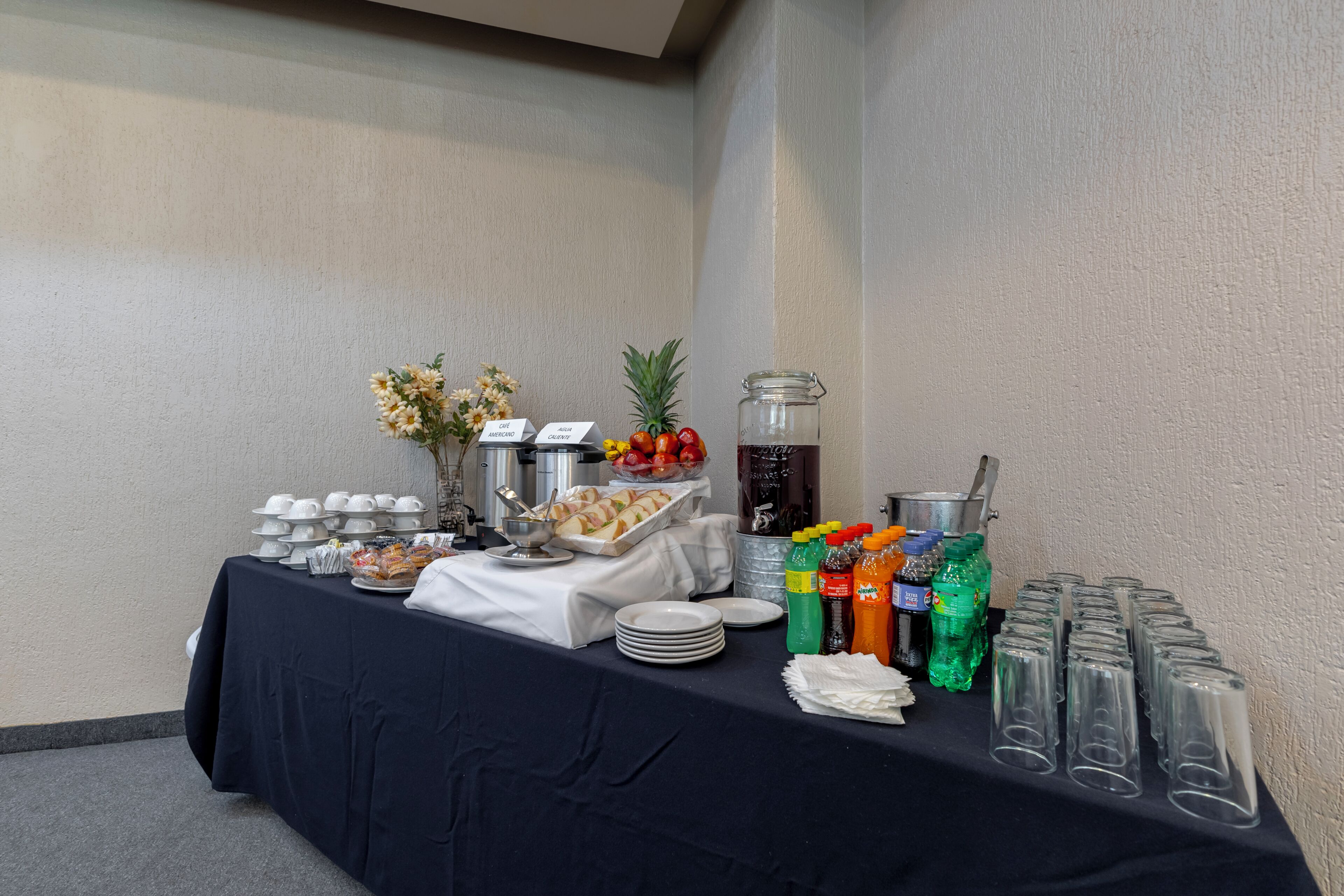 Una mesa de buffet con diversos alimentos, un dispensador de agua y botellas de bebidas.