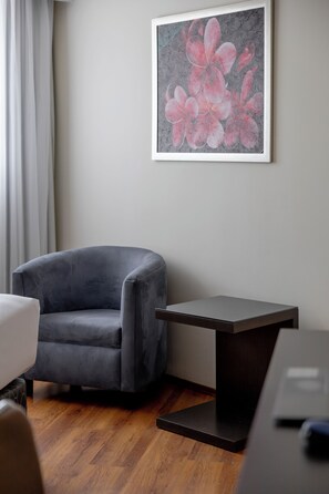 Una habitación con un sillón gris, una mesita pequeña y una obra de arte enmarcada en la pared.