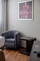 Una habitación con un sillón gris, una mesita pequeña y una obra de arte enmarcada en la pared.