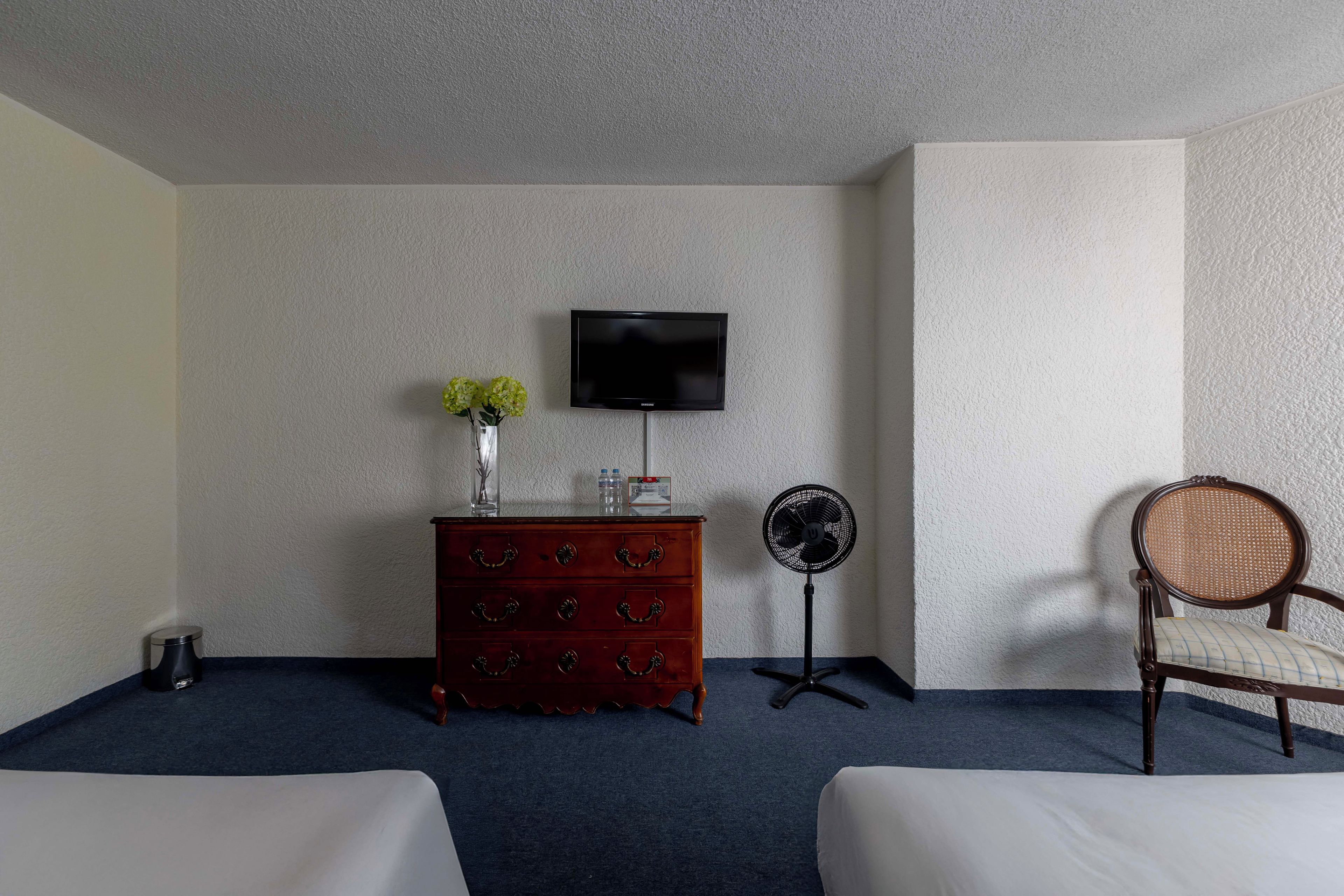Une chambre d’hôtel avec deux lits, une commode en bois, une télévision, un ventilateur et une chaise.