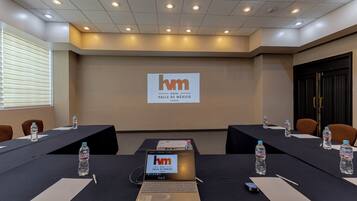 A conference room with a large screen displaying the hotel name, tables with water bottles, and laptops.
