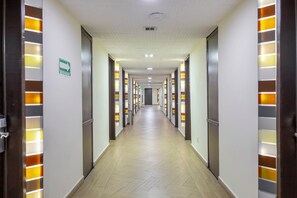 A hotel corridor with doors on both sides, illuminated by vertical light panels, and a sign indicating an evacuation route. - Hotel Valle de Mexico Toreo (Naucalpan)