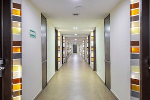 A hotel corridor with doors on both sides, illuminated by vertical light panels, and a sign indicating an evacuation route.