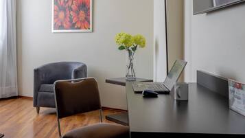 Ein modernes Zimmer mit Schreibtisch, Stuhl, Laptop und einer Vase mit Blumen.