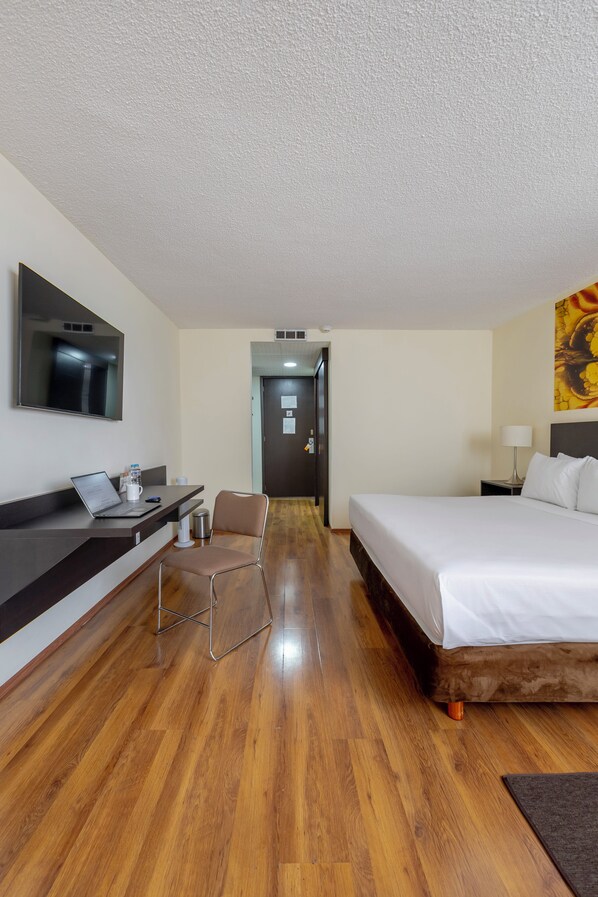 Habitación de hotel con cama, escritorio, laptop, silla y televisión en la pared.