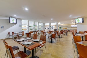Un comedor amplio con múltiples mesas y sillas, equipado con televisores de pantalla plana en las paredes.