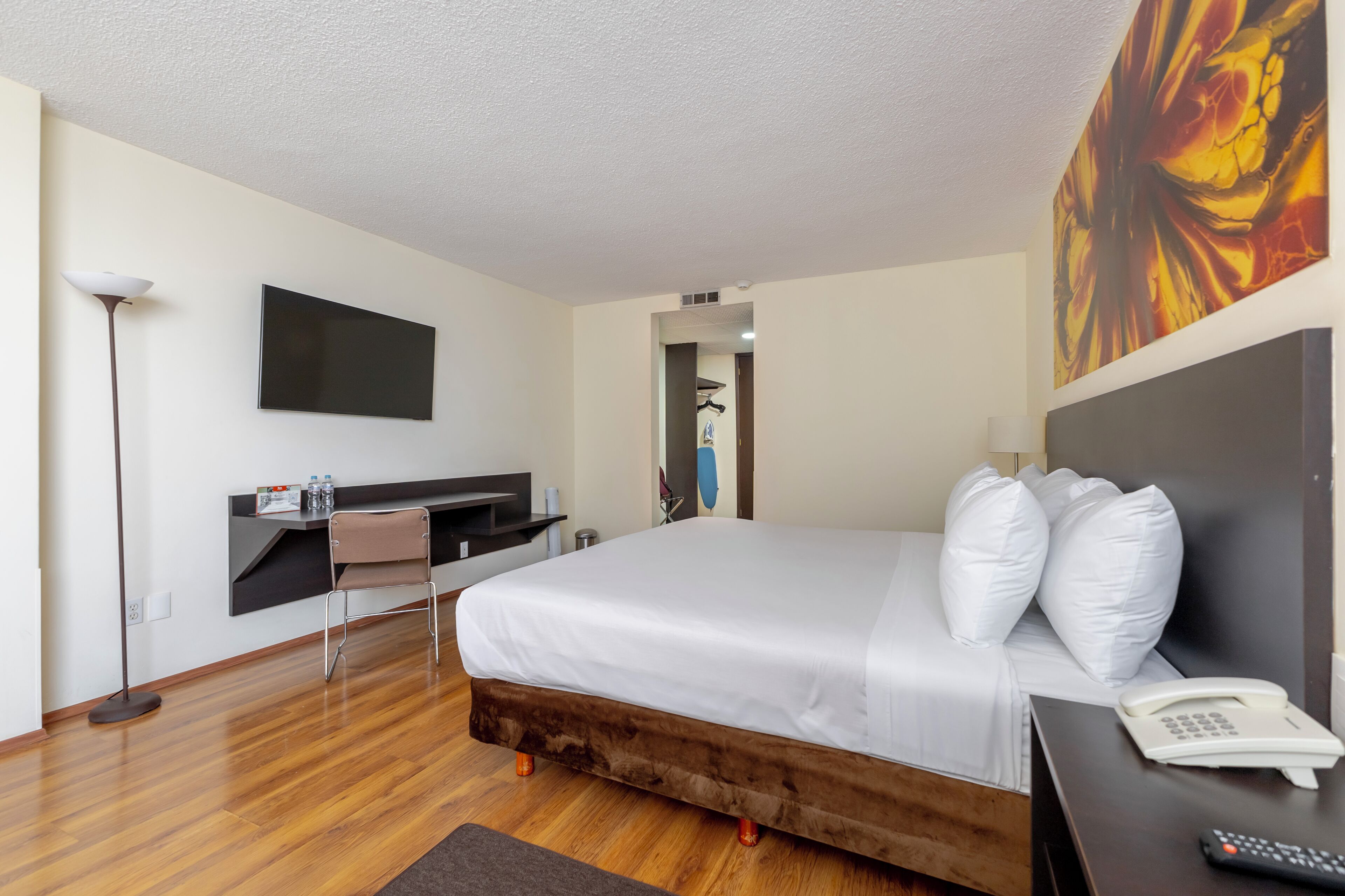 A hotel room with a bed, bedside table, lamp, and a painting on the wall.
