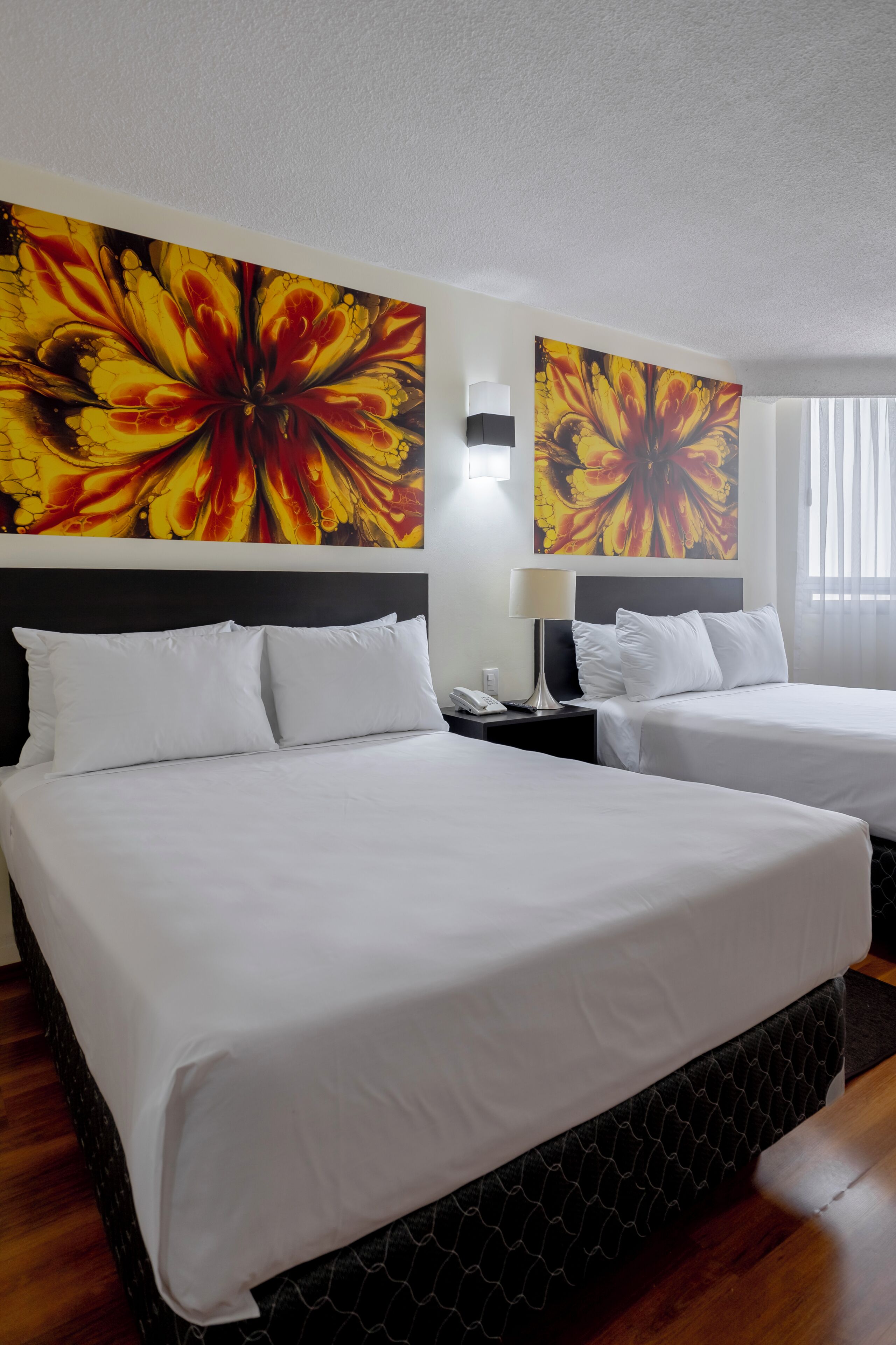 A hotel room with two beds, a large floral artwork on the wall, a bedside lamp, and a phone on the nightstand.
