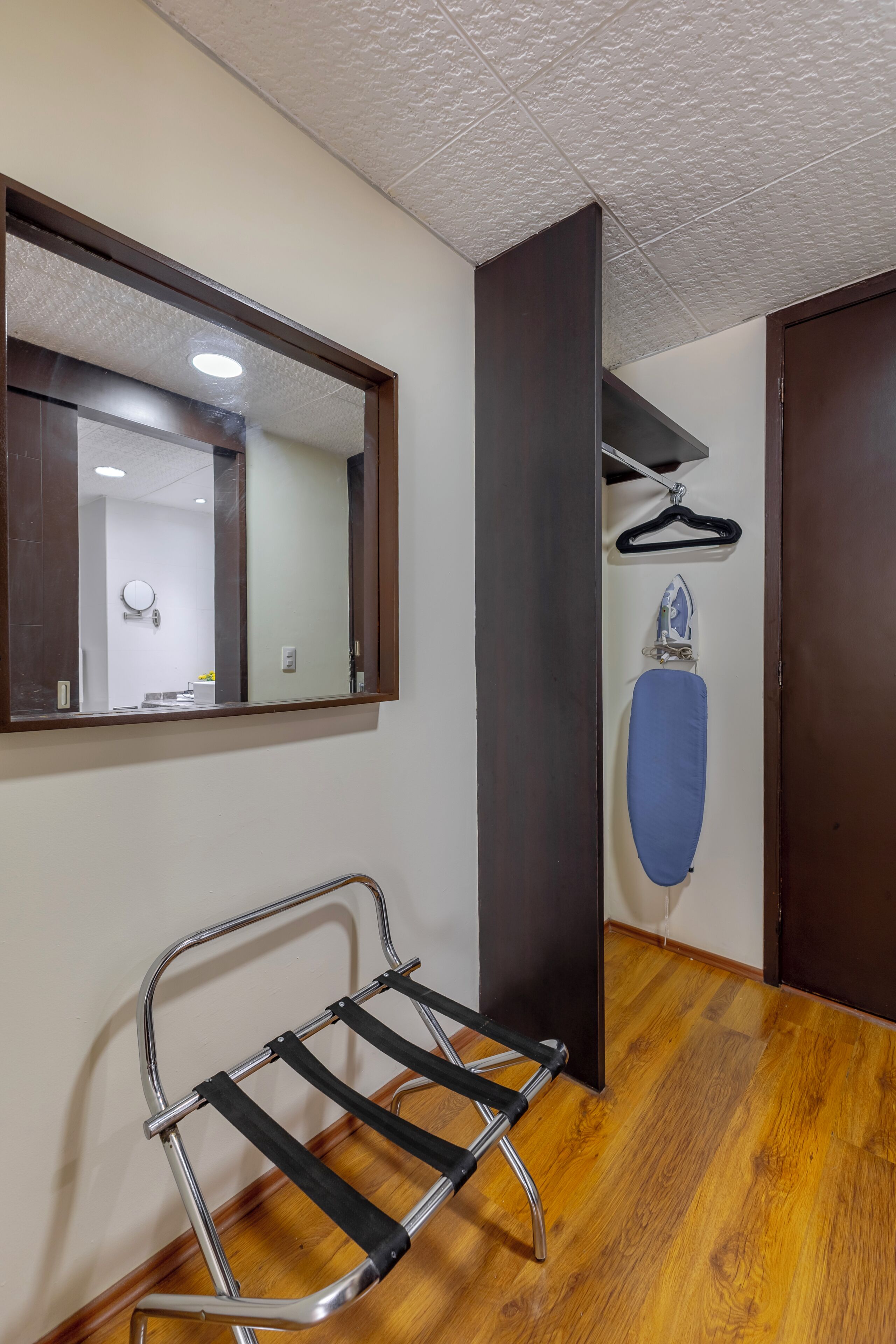 Una habitación con suelo de madera, un perchero metálico, un espejo y una puerta.