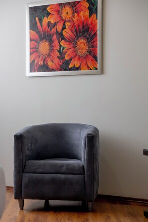 Un sillón gris oscuro en una habitación con suelo de madera y un cuadro enmarcado de flores naranjas en la pared.