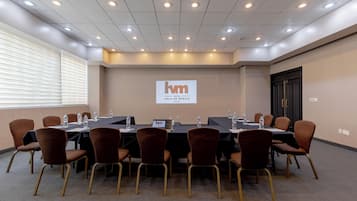 A conference room with a long table, chairs, and a projector screen displaying the hotel name.