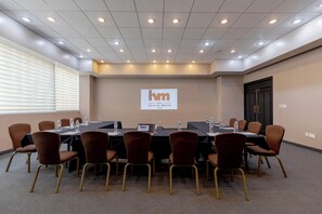 Un salón de conferencias con una larga mesa, sillas y una pantalla que muestra el nombre del hotel.