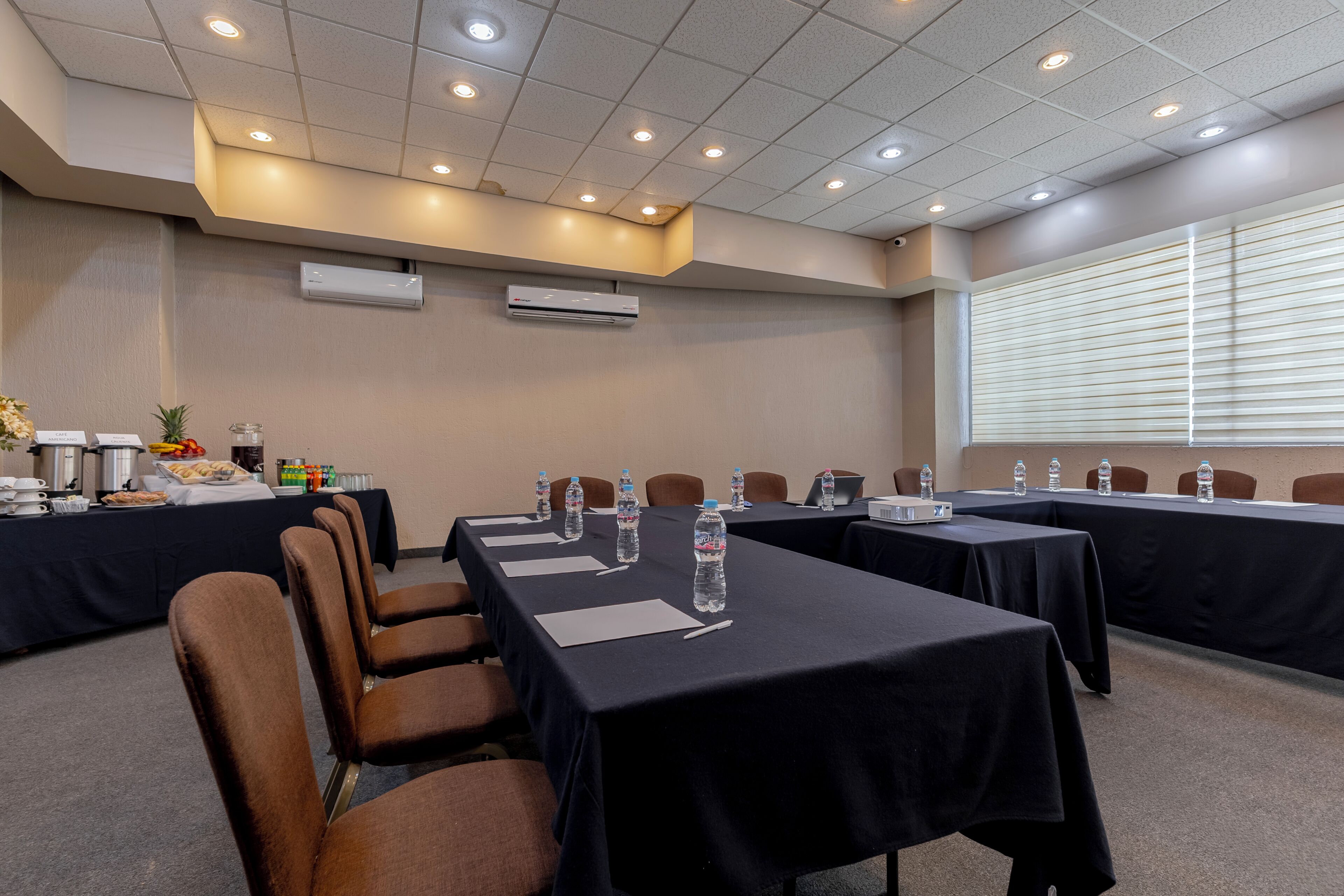 Un salón de conferencias con mesas, sillas, botellas de agua y un proyector.