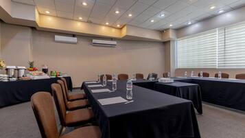 Un salón de conferencias con mesas, sillas, botellas de agua y un proyector.