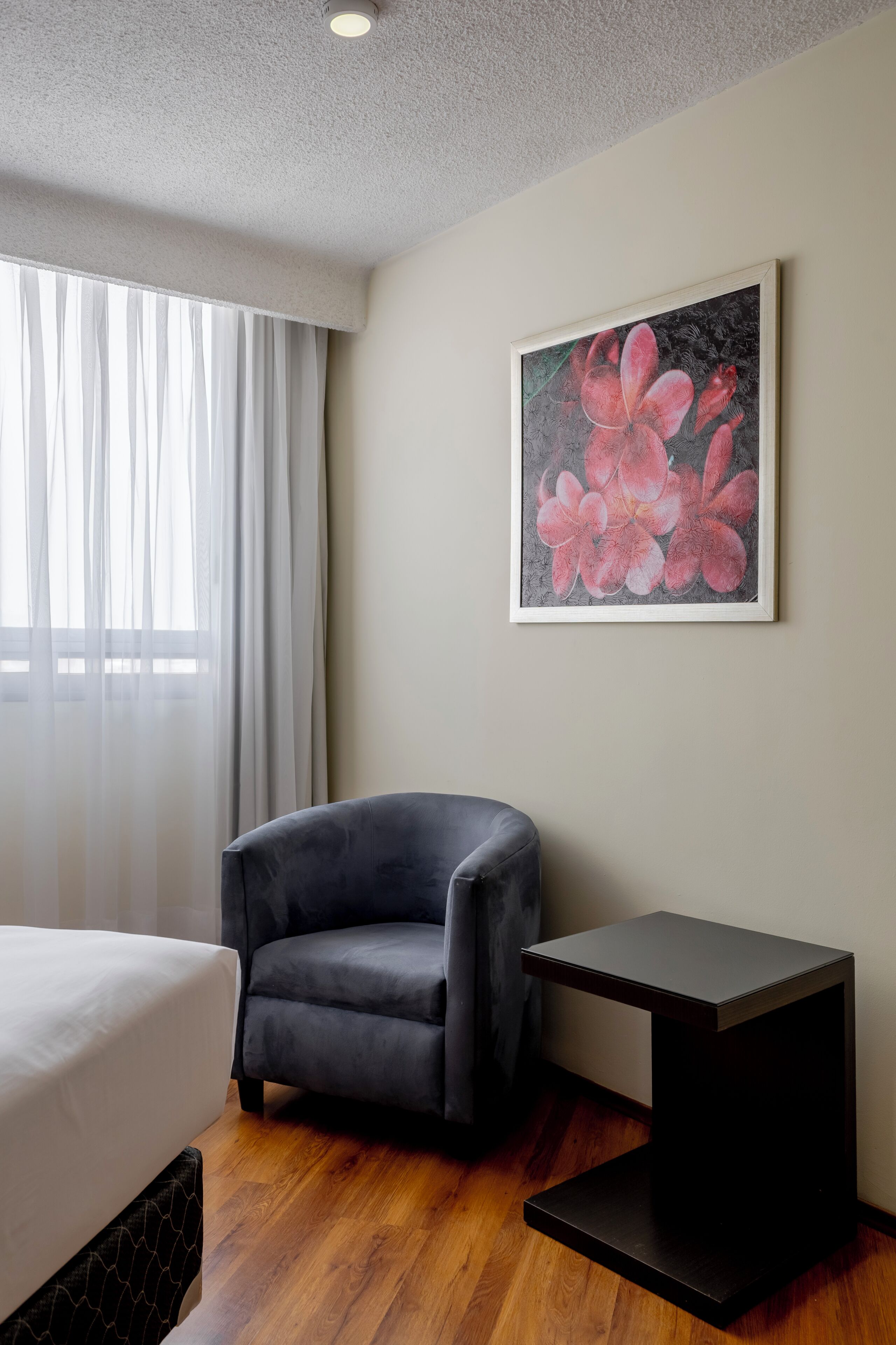 Una habitación de hotel con una cama, una silla, una mesita y un cuadro en la pared.