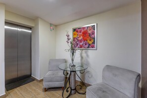 A room with a grey sofa, a glass table with a vase of flowers, and a colorful painting on the wall. - Hotel Valle de Mexico Toreo (Naucalpan)