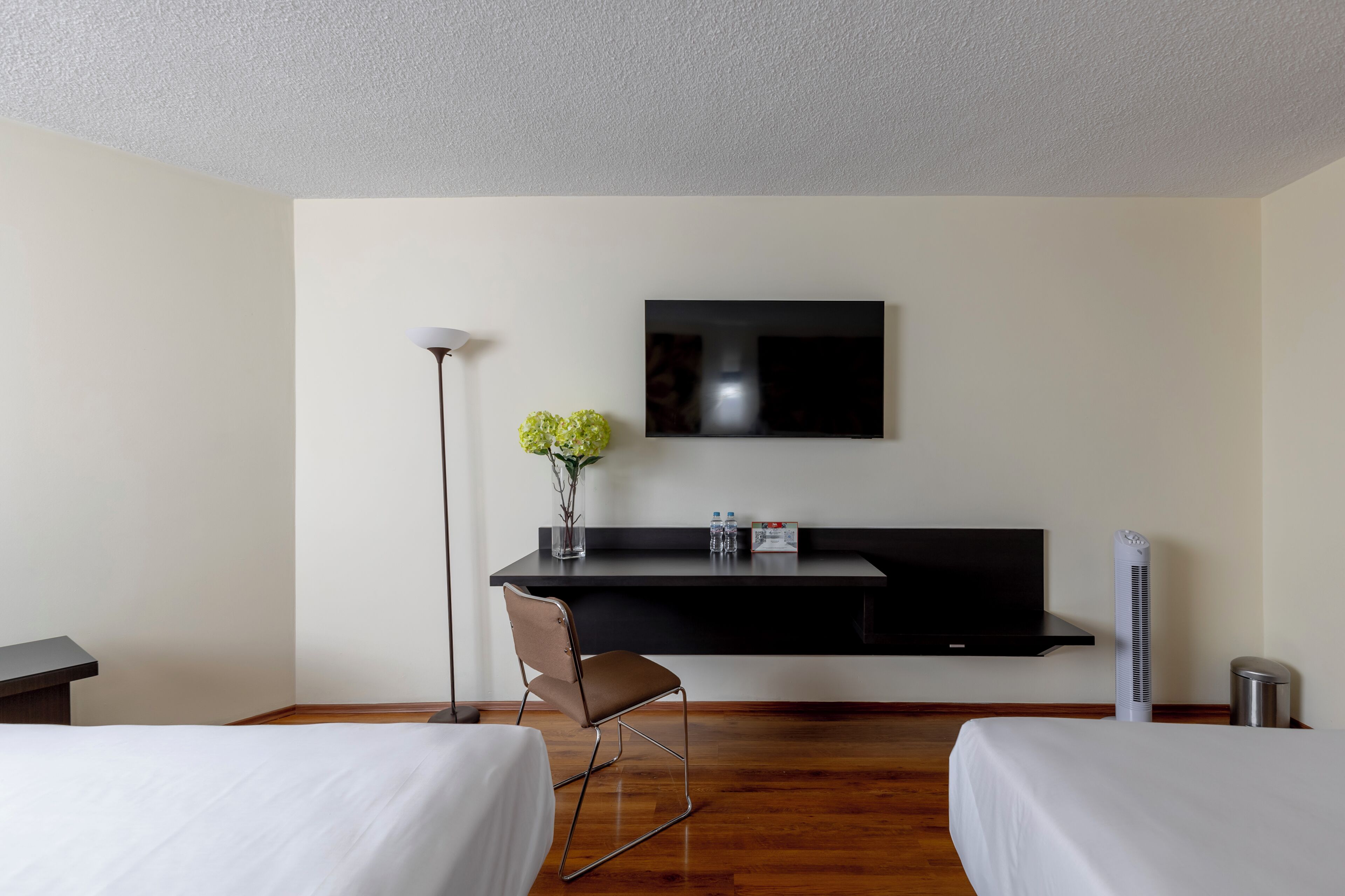 Habitación de hotel con dos camas, un escritorio, un televisor de pantalla plana, un florero con flores, una silla y un calefactor portátil.