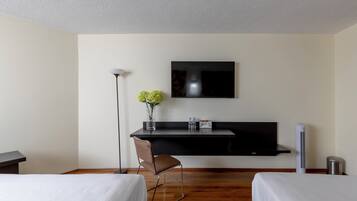 Habitación de hotel con dos camas, un escritorio, un televisor de pantalla plana, un florero con flores, una silla y un calefactor portátil.