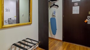 A room with a wooden floor, a mirror with a gold frame, a black ironing board, and a door with a hanging paper. - Hotel Valle de Mexico Toreo (Naucalpan)