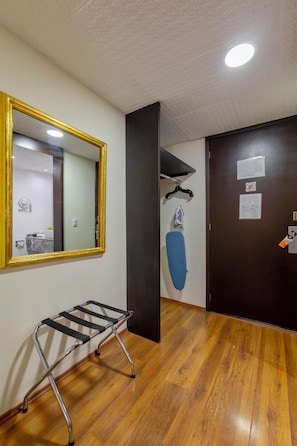 Una habitación con piso de madera, un espejo de marco dorado, una plancha negra y una puerta con un papel colgante.
