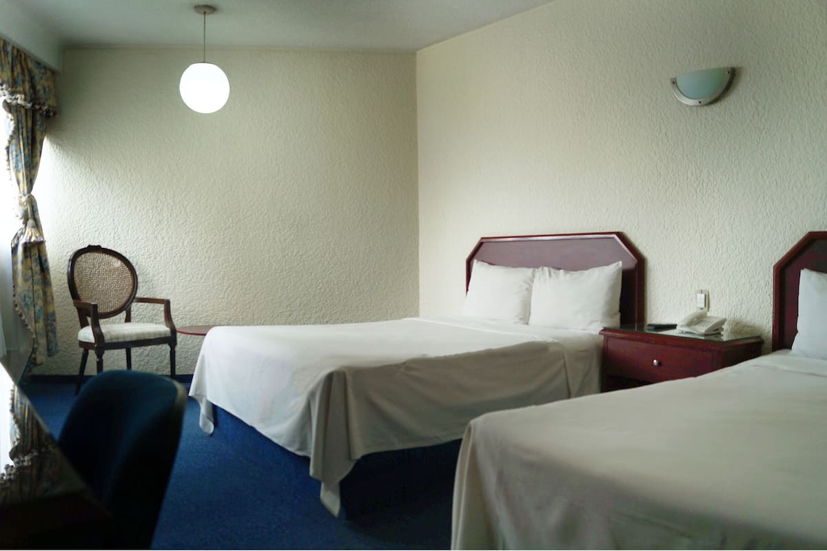 A hotel room with two single beds, a wooden nightstand, a chair, and a hanging light fixture.