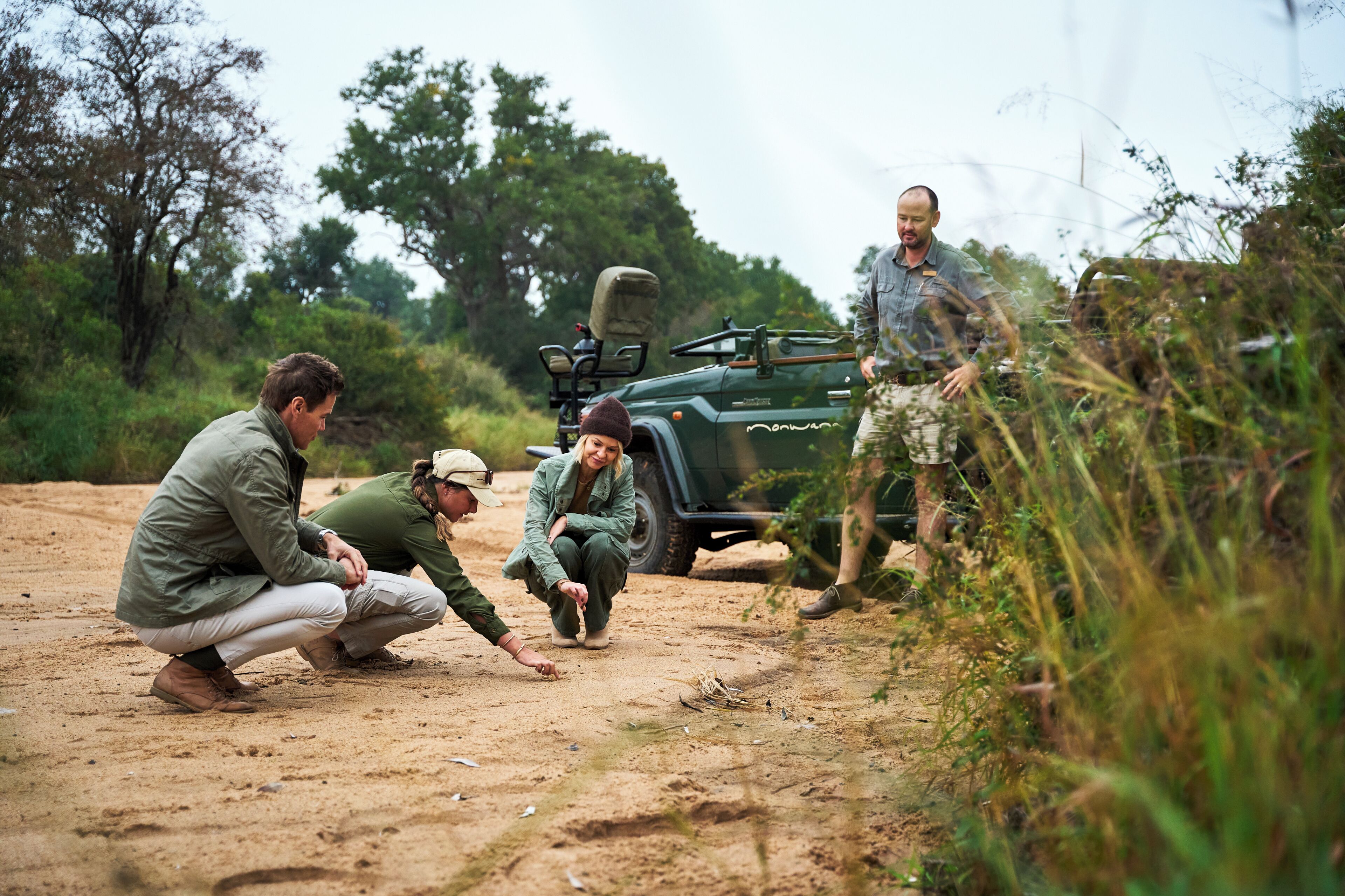 A group of people in outdoor attire, examining the ground near a vehicle.