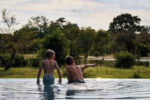 Dos personas en una piscina, con un paisaje natural al fondo.