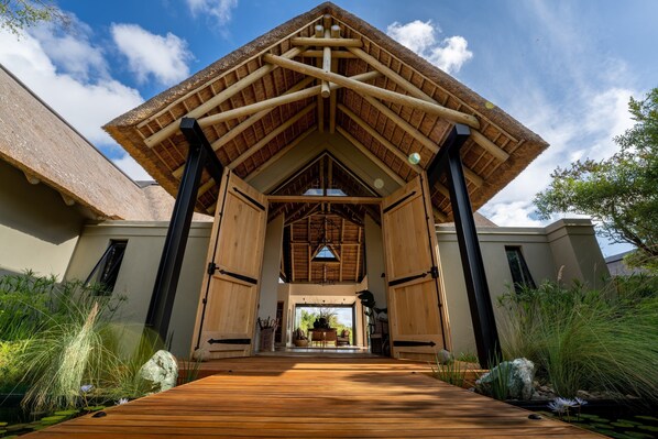 A wooden structure with a thatched roof, leading to a covered outdoor area with a table and chairs. - Monwana (Hoedspruit)