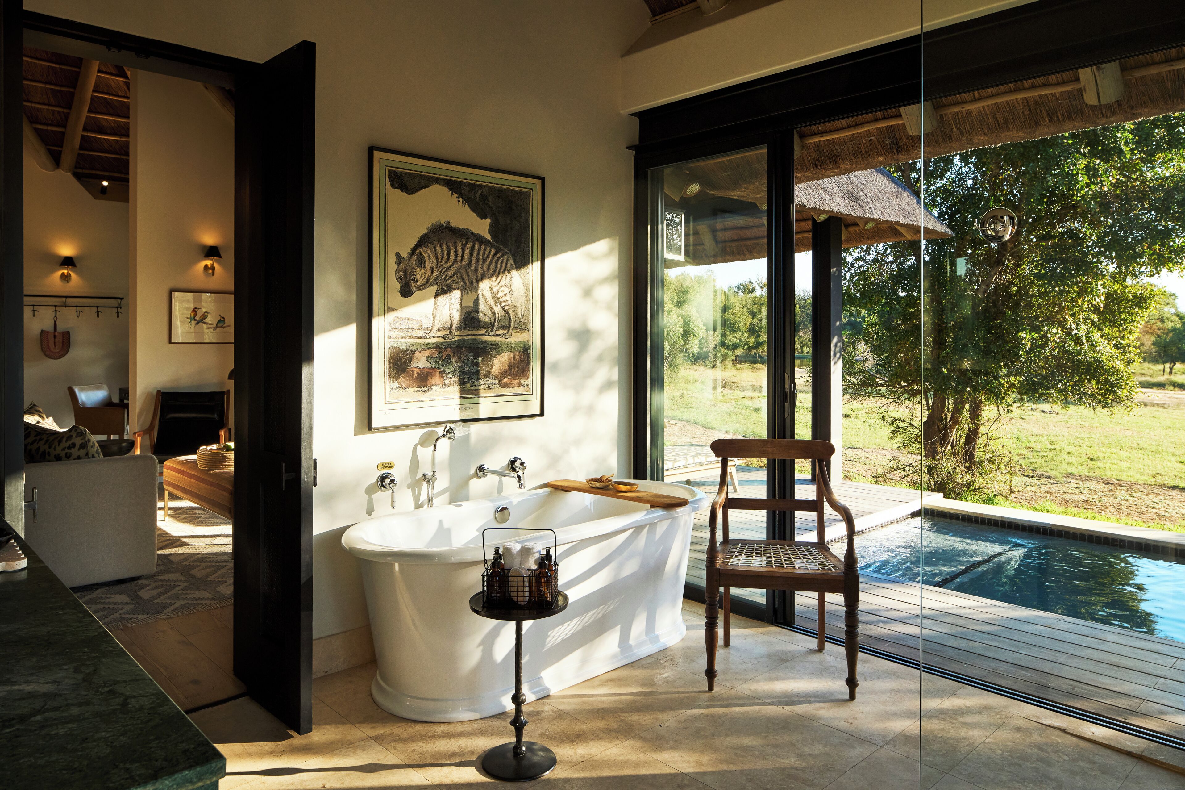 A modern bathroom with a freestanding bathtub, a wooden chair, and a large window overlooking a pool.
