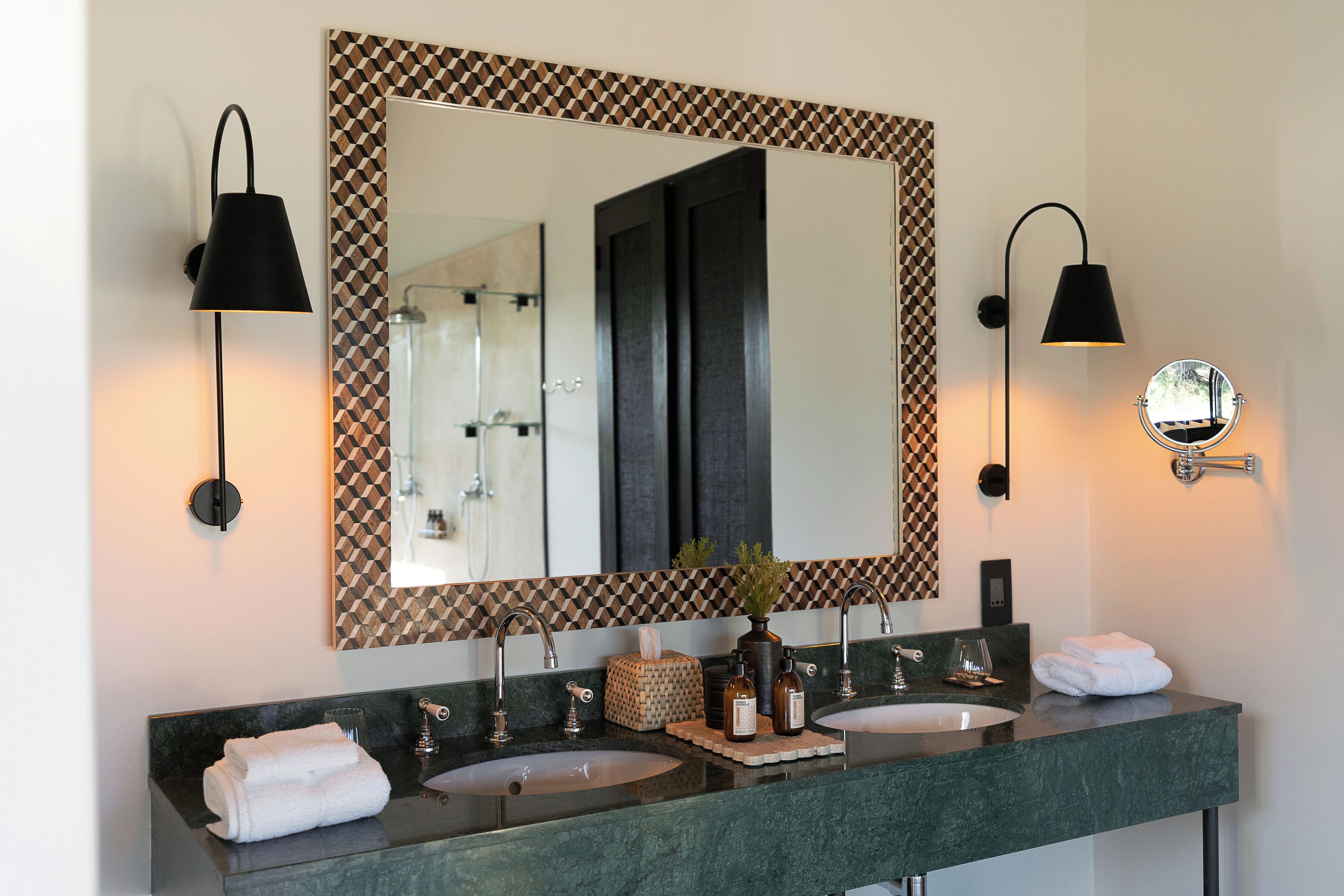 A bathroom with two sinks, a large mirror with a geometric frame, and wall-mounted lighting.