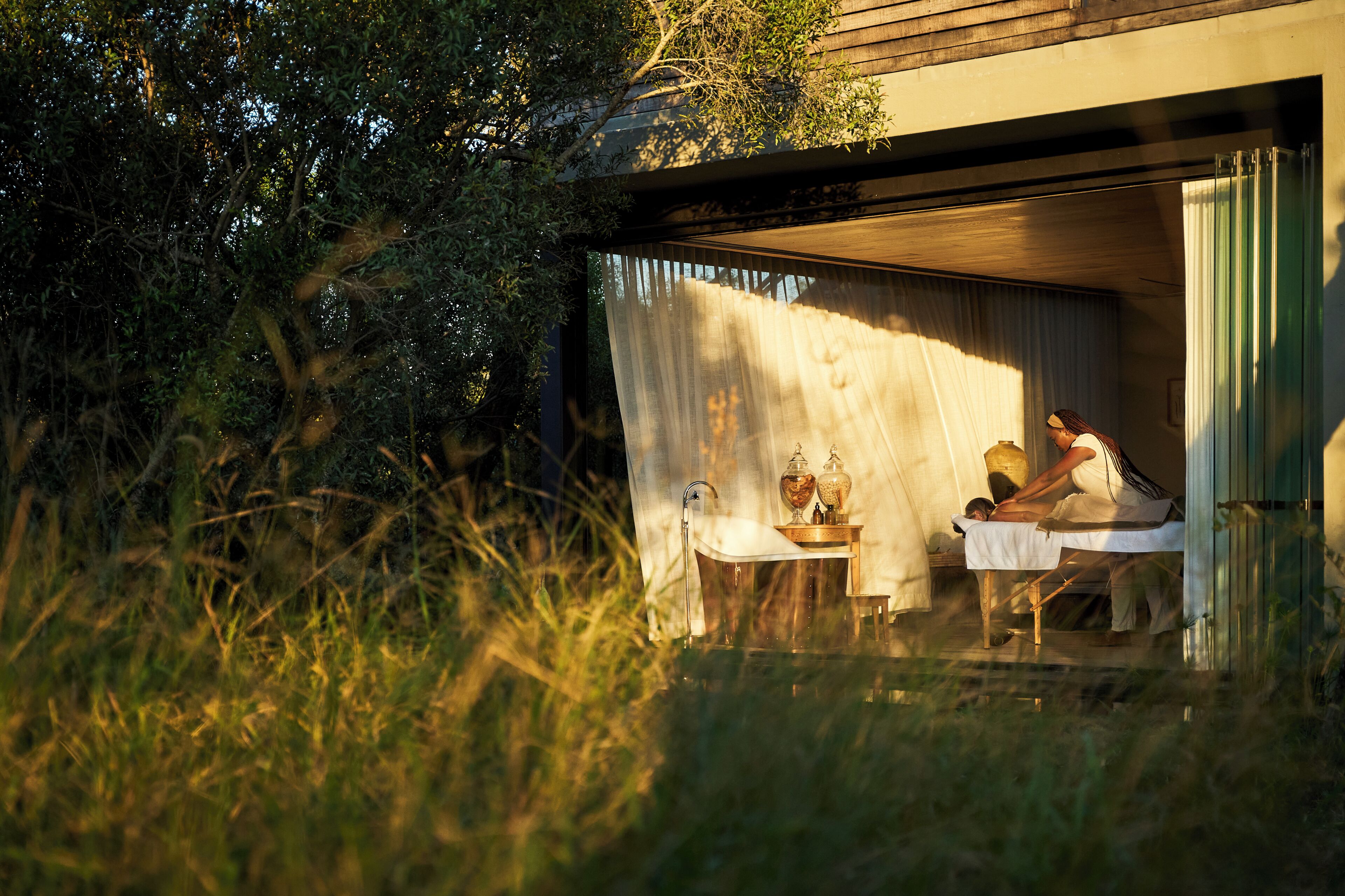 An outdoor spa area with a wooden deck, a table with a towel, and a person receiving a massage.