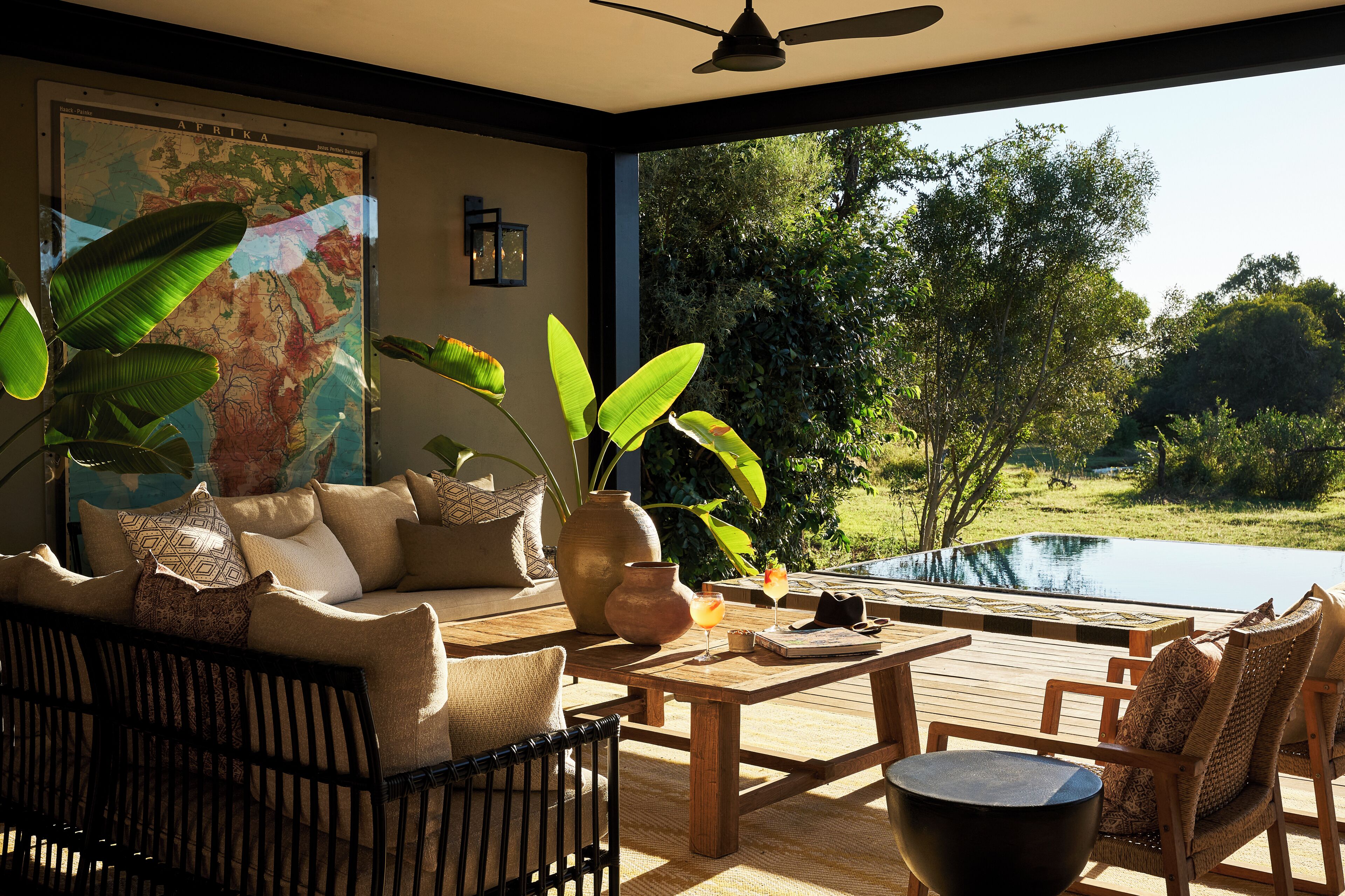 A room with a large window, a map on the wall, a sofa, a coffee table, and a view of a pond.