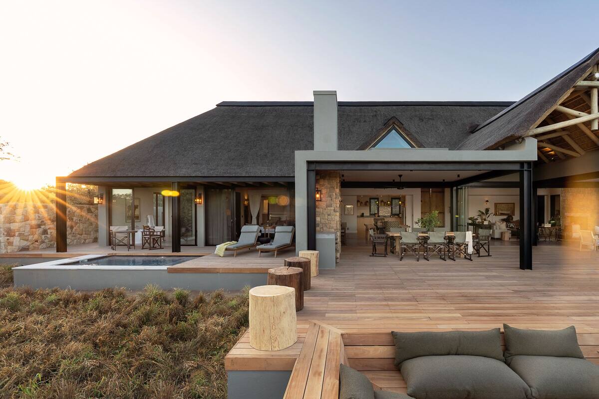 A modern house with a large deck, outdoor seating, and a swimming pool.