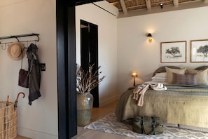 A bedroom with a bed, bedside lamps, a nightstand, a vase with branches, a wicker basket, and a hat on the wall.