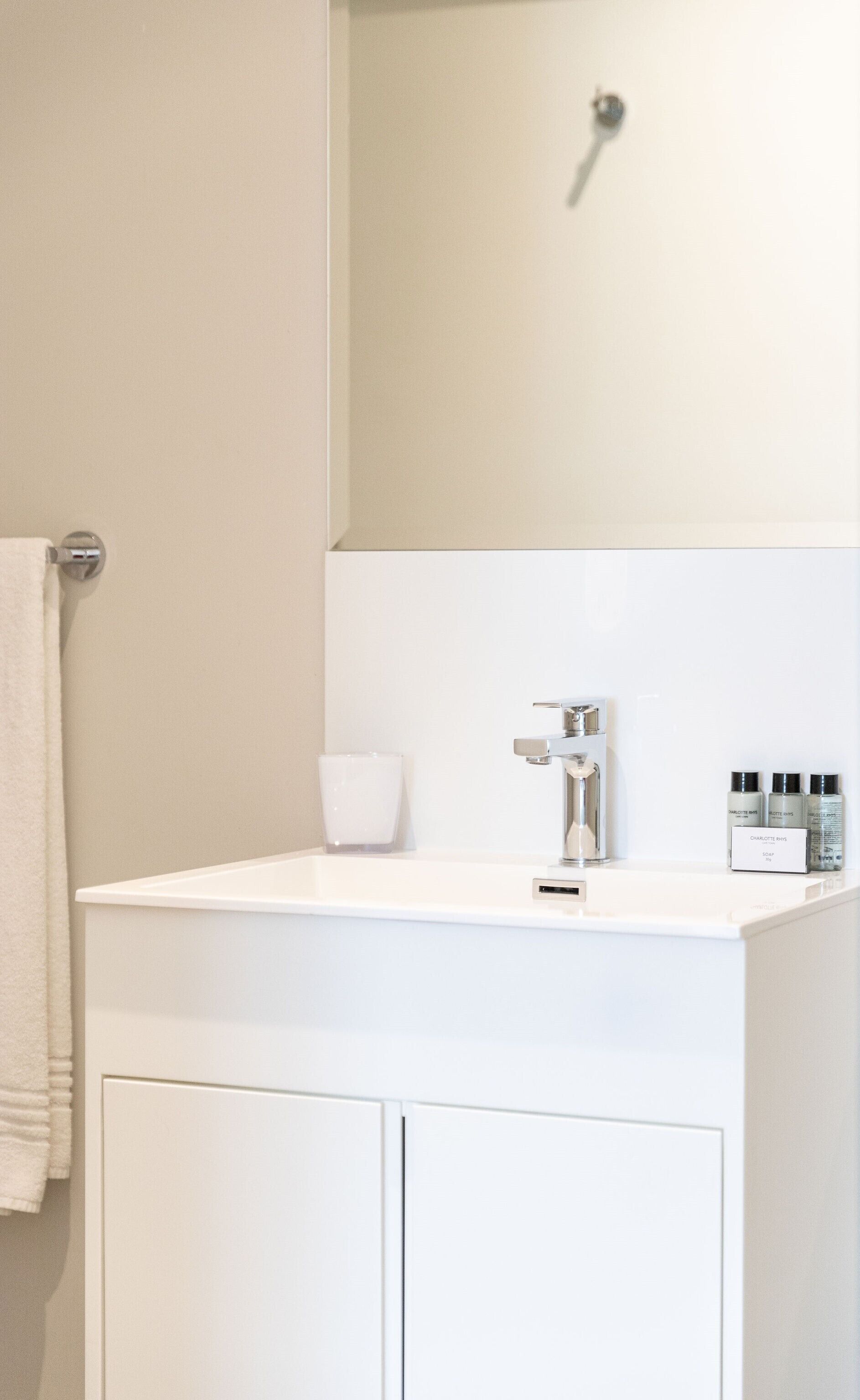 A bathroom with a white sink, a glass cup, and toiletries on the counter.