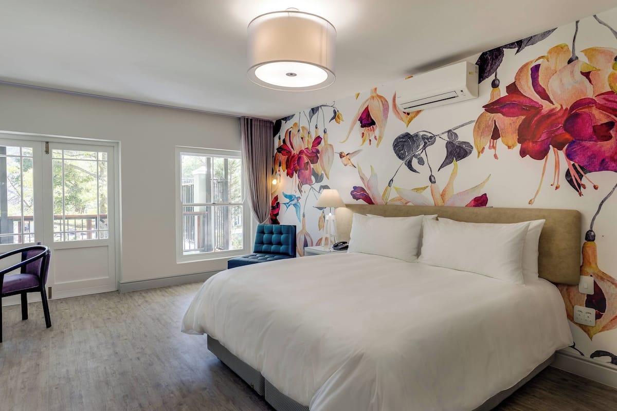 A bedroom with a large bed, a chair, a nightstand, and a wall with a floral mural.