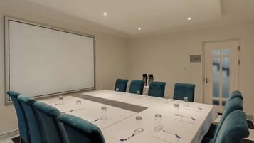 Una sala de conferencias con una larga mesa, sillas azules y una pantalla para proyector.