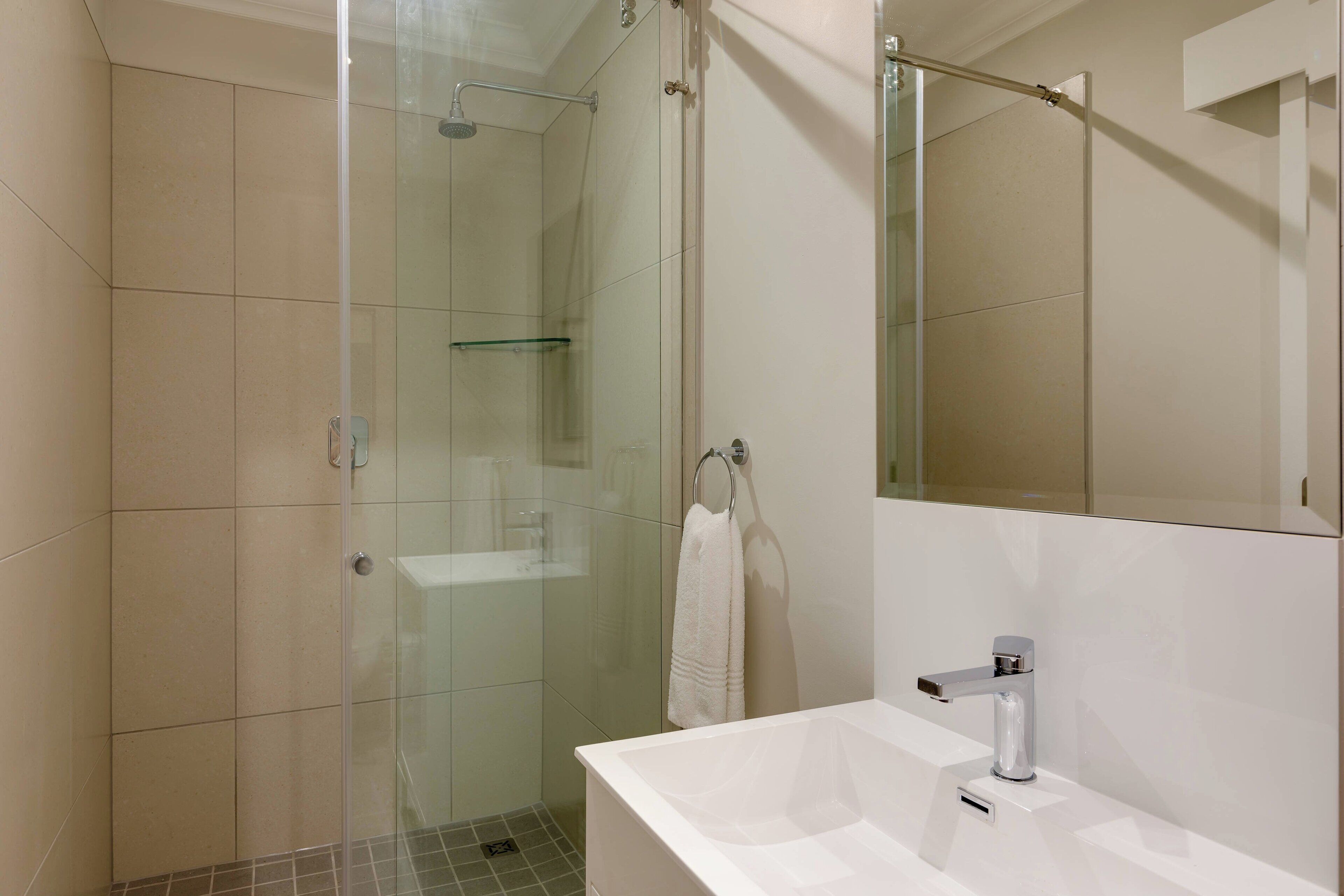 Une salle de bain moderne avec une douche à parois de verre, un lavabo blanc et un grand miroir.