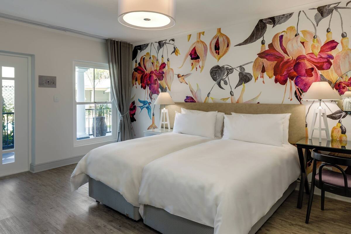 A hotel room with a large bed, a desk with a chair, and a window with curtains.