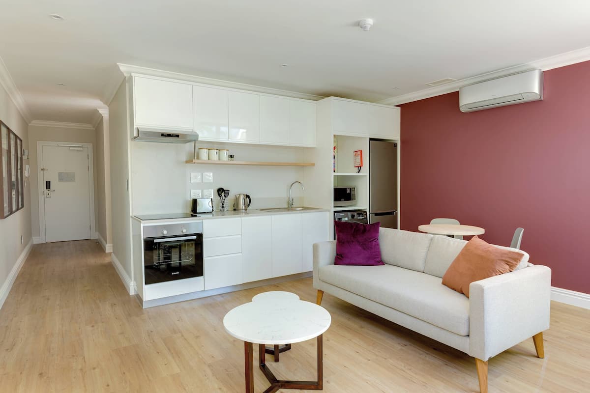 A modern kitchen with white cabinets, a built-in oven, and a dining area with a white table and a beige sofa.