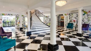 A lobby with a black and white checkered floor, a staircase, and floral wallpaper.