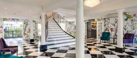 A lobby with a black and white checkered floor, a staircase, and floral wallpaper.