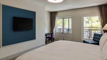 Une chambre d’hôtel avec un grand lit, un téléviseur à écran plat fixé à un mur bleu, un bureau avec une chaise et une vue sur l’extérieur par une fenêtre.