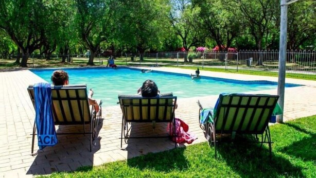Un área de piscina con tres sillas de descanso, un espacio de estar cubierto y una piscina cercada.