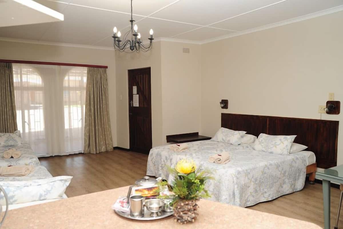 A hotel room with two beds, a chandelier, a dining table with a tray of breakfast items, and a window with curtains.
