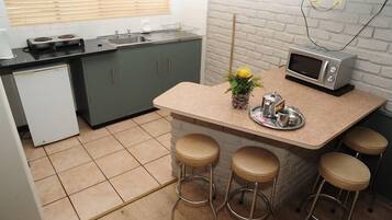 Una cocina compacta equipada con microondas, un refrigerador pequeño y una zona de bar con taburetes.
