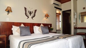 Habitación de hotel con una cama grande, dos mesitas de noche, cabecero de madera, lámparas fijadas a la pared y una decoración de mariposa.