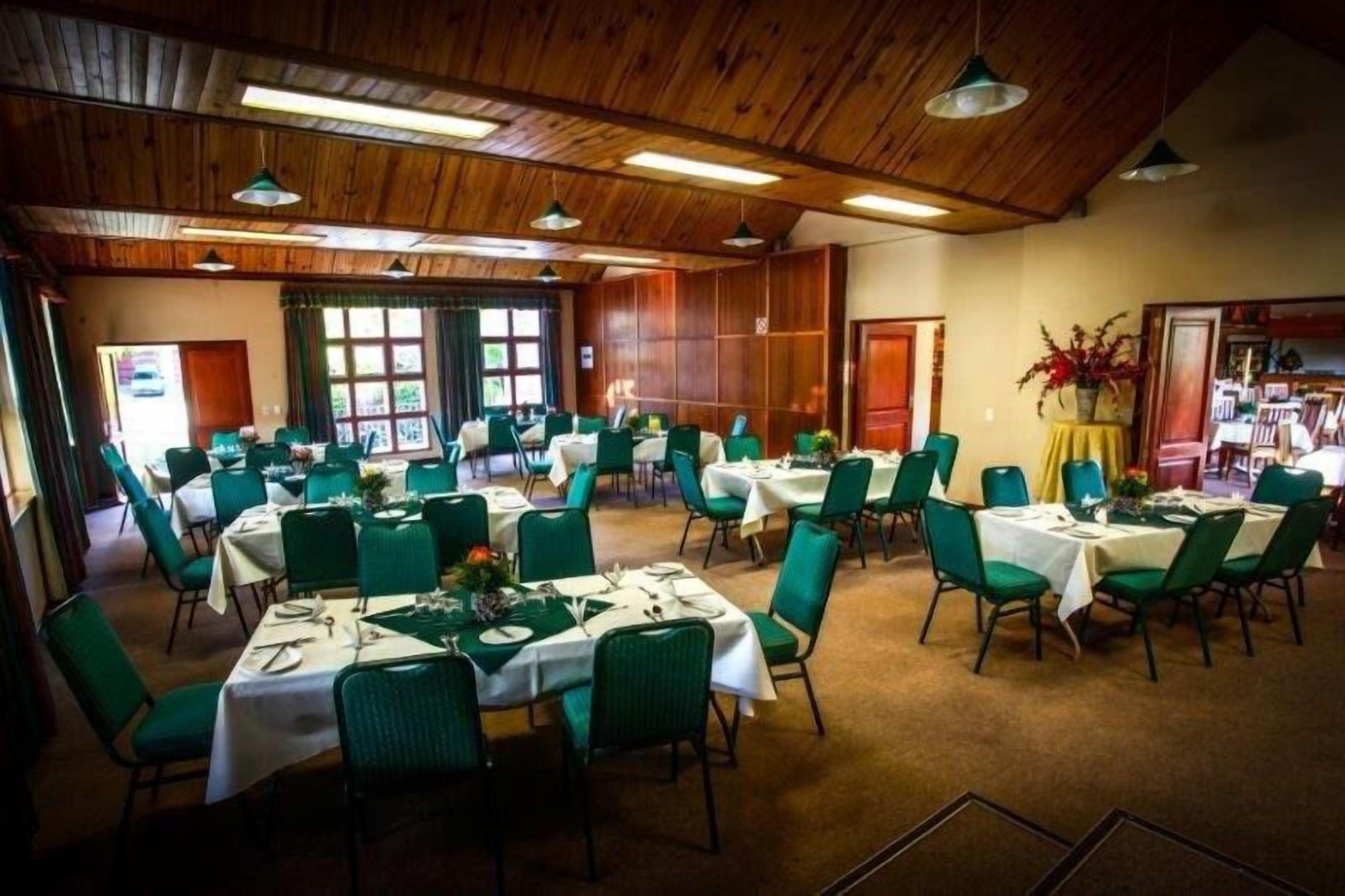 Un comedor con varias mesas y sillas, techo de madera y ventanas amplias.