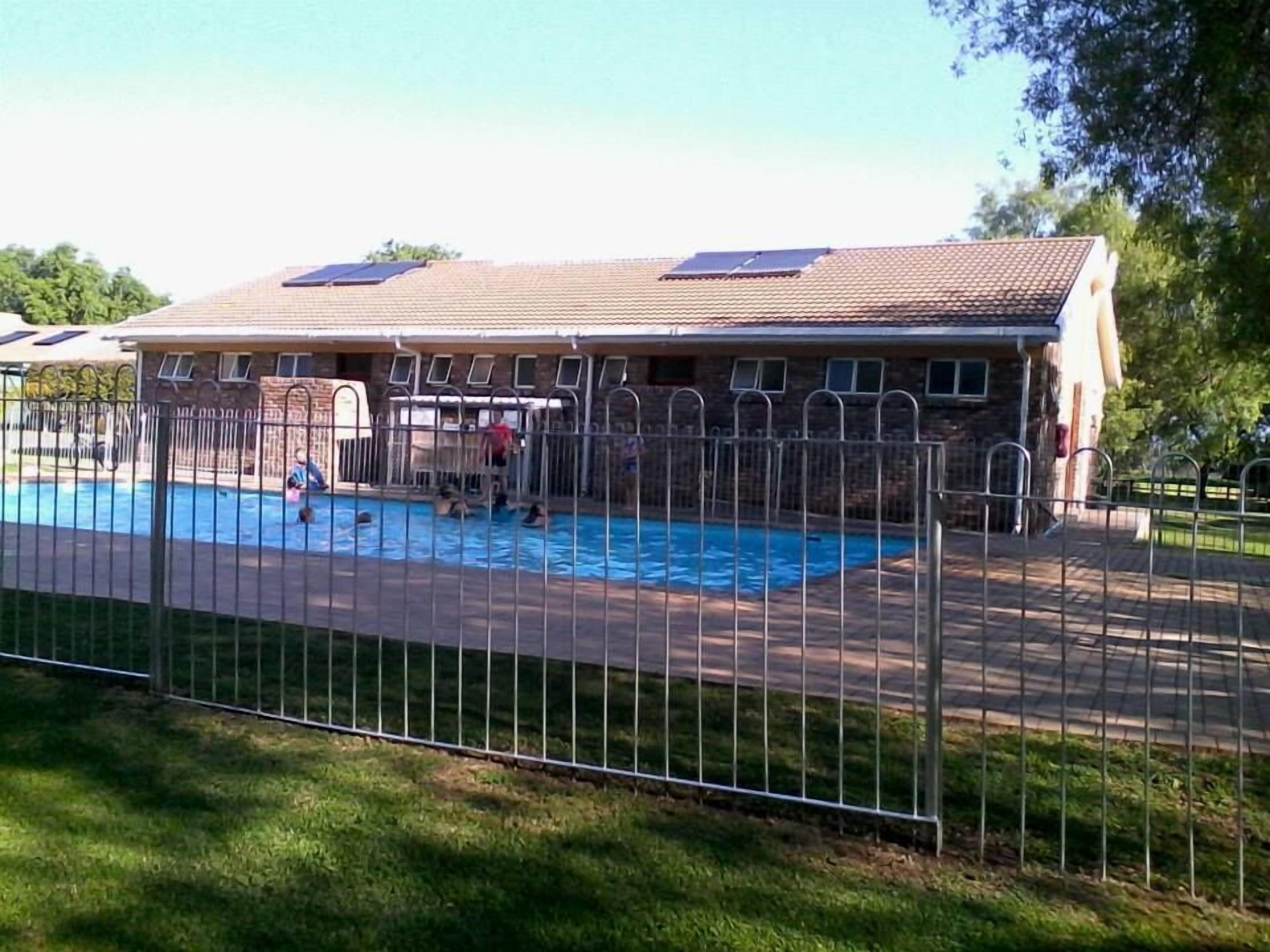 En swimmingpool med ett inhägnat område, omgiven av en byggnad med ett tak täckt av tegelpannor och fönster.