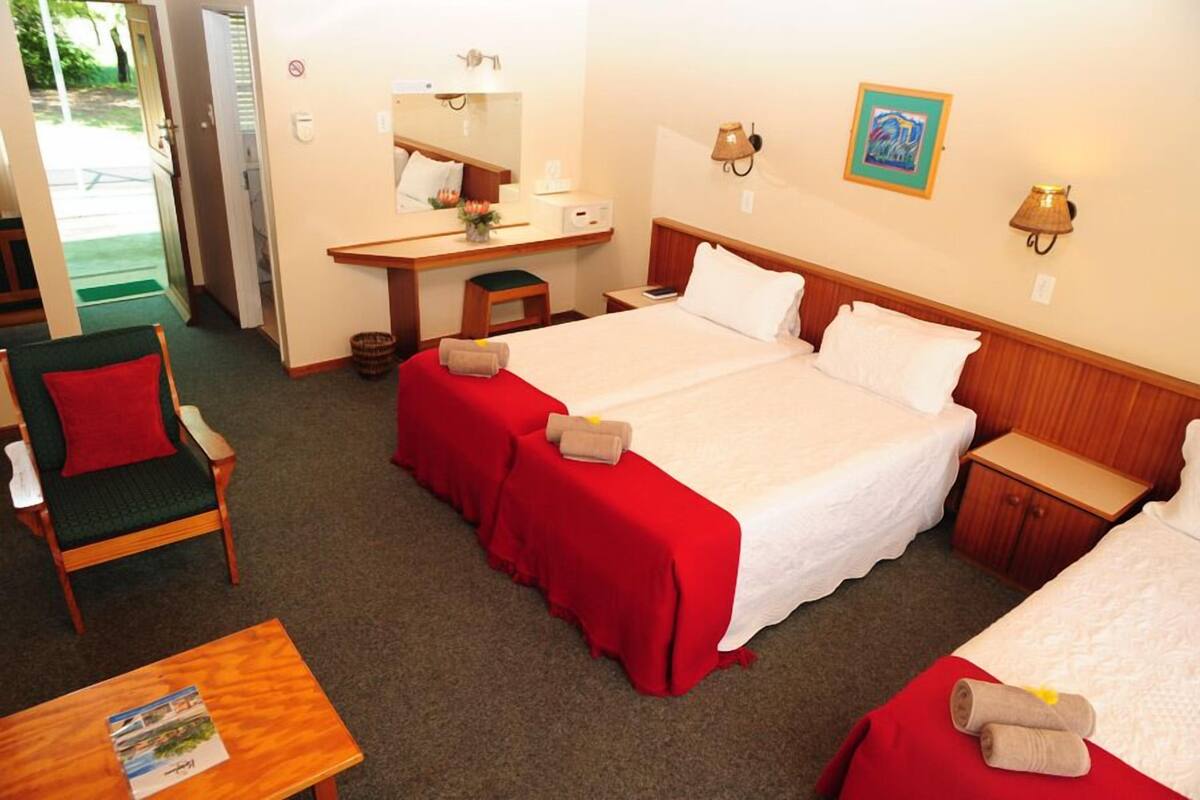 A hotel room with two beds, a desk, a chair, and a small table.